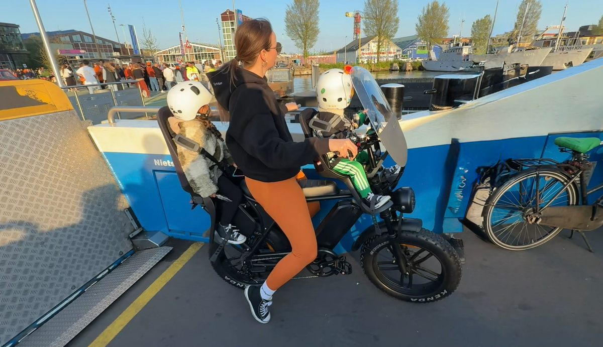 A woman cycling with two helmeted children aboard a ferry